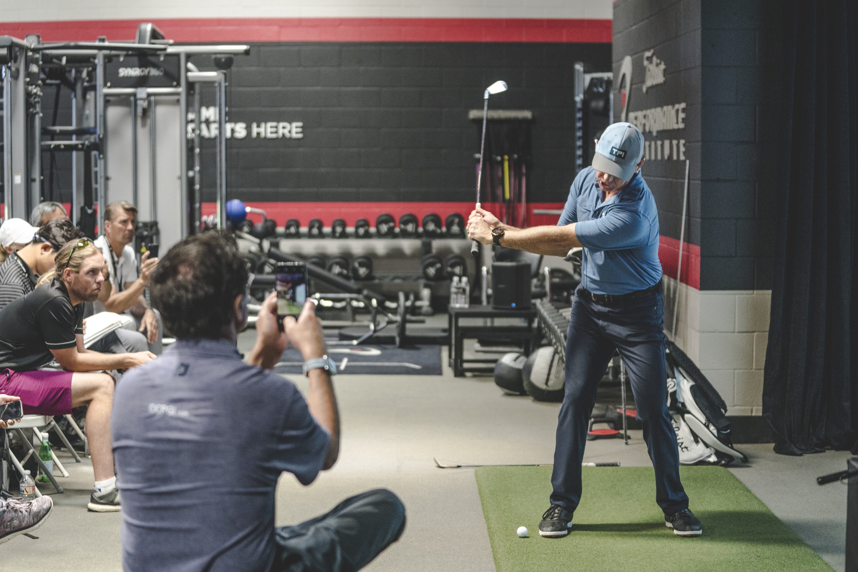 Golfer demonstrating swing indoors to seated audience