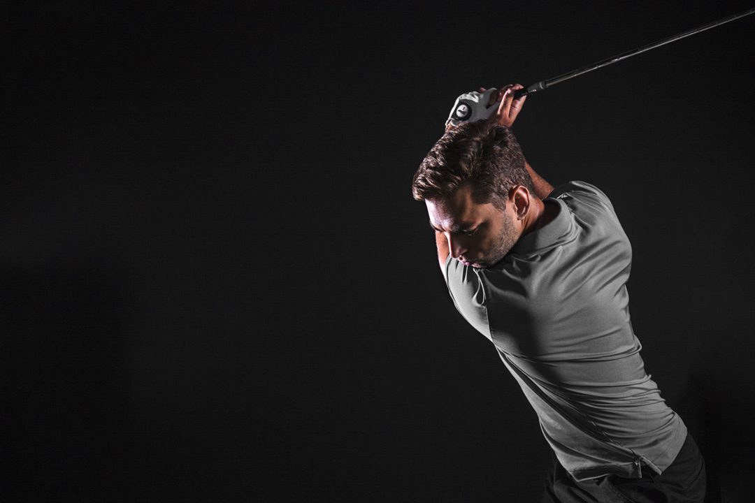 Man swinging golf club against dark background