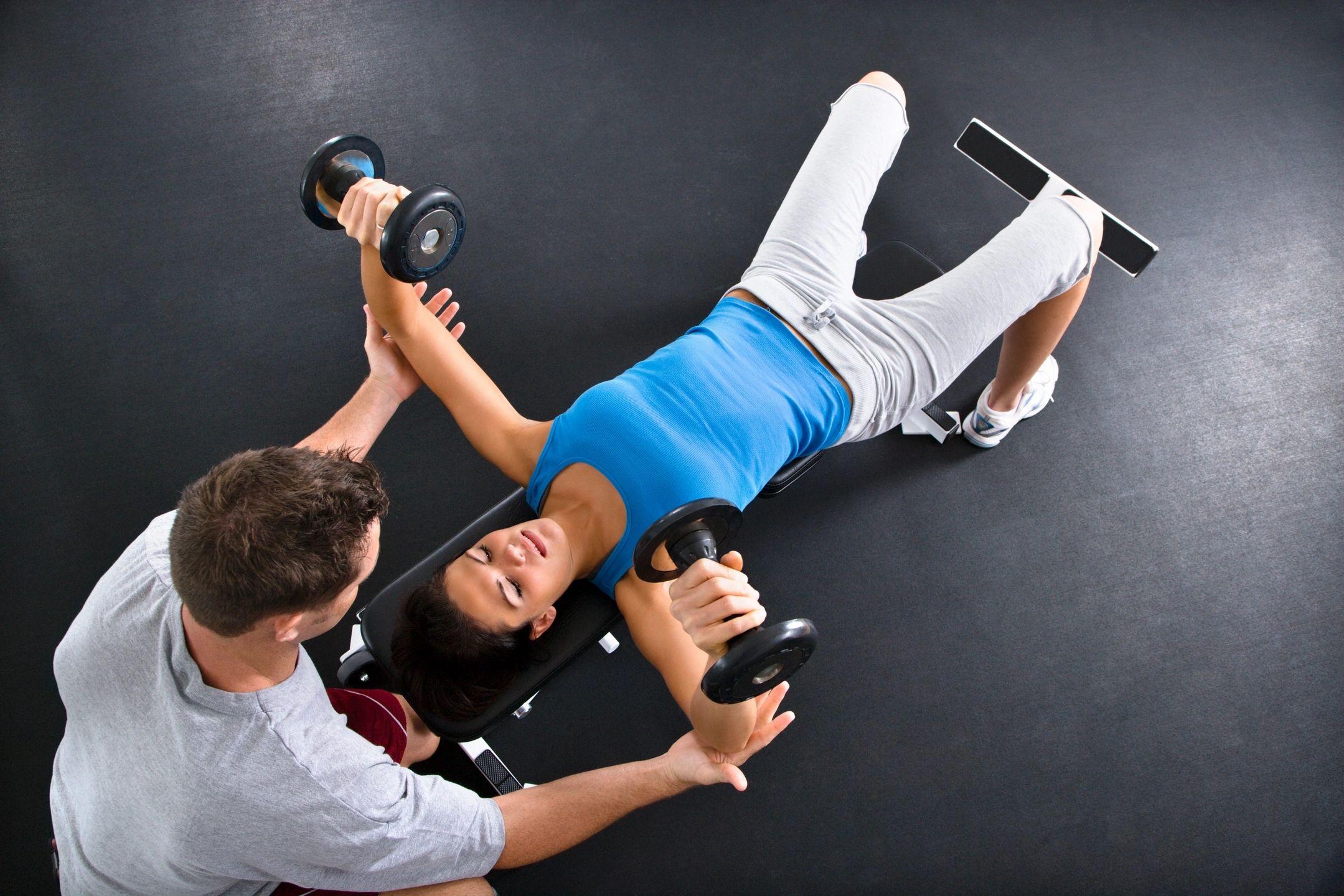 Woman doing dumbbell bench press with trainer