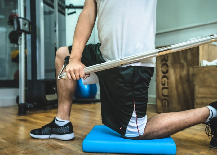 Person kneeling on blue pad holding barbell